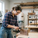 Jeune femme examine un échantillon de bois dans un atelier de menuiserie