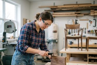 Jeune femme examine un échantillon de bois dans un atelier de menuiserie